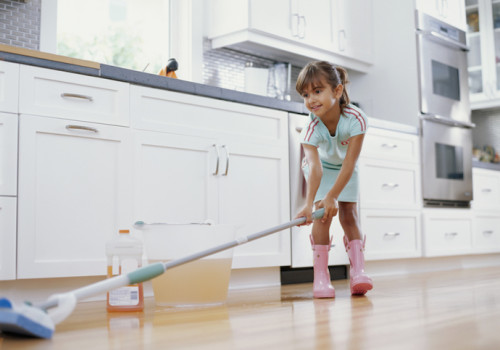 Girl (6-8) cleaning kitchen floor with mop, smiling, low angle view