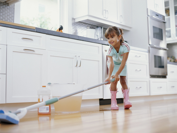 Girl (6-8) cleaning kitchen floor with mop, smiling, low angle view
