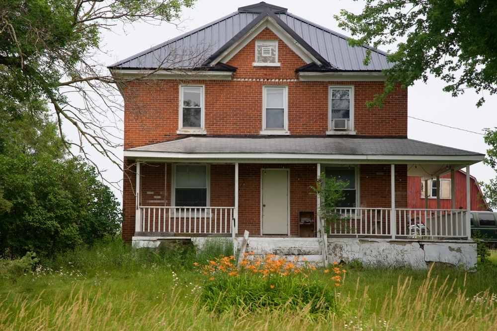 older brick farmhouse with overgrown yard